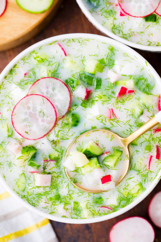 Overhead shot of a bowl of creamy Russian okroshka made with fresh cucumbers and radishes.
