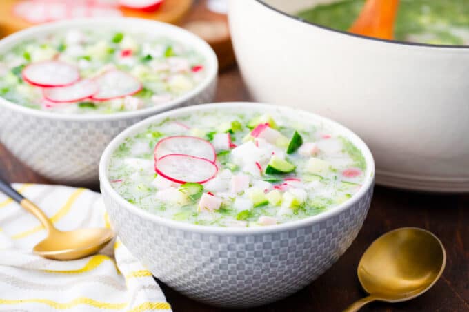 A bowl of cold summer soup Russian okroshka made with fresh cucumbers and radishes.