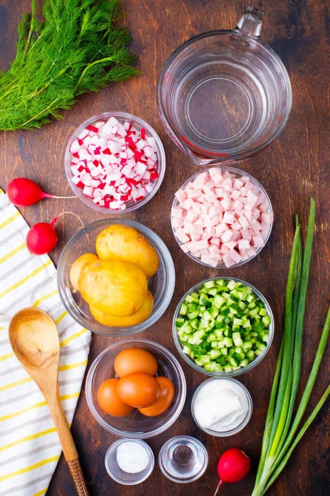 Overhead shot of cold summer soup Russian okroshka ingredients in bowls on a table.
