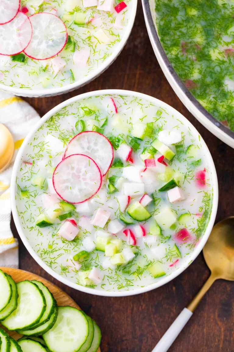 Overhead shot of a bowl of cold summer soup Russian okroshka made with fresh cucumbers and radishes.
