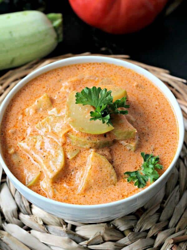 Creamy zucchini tomato soup garnished with chopped parley in a white bowl