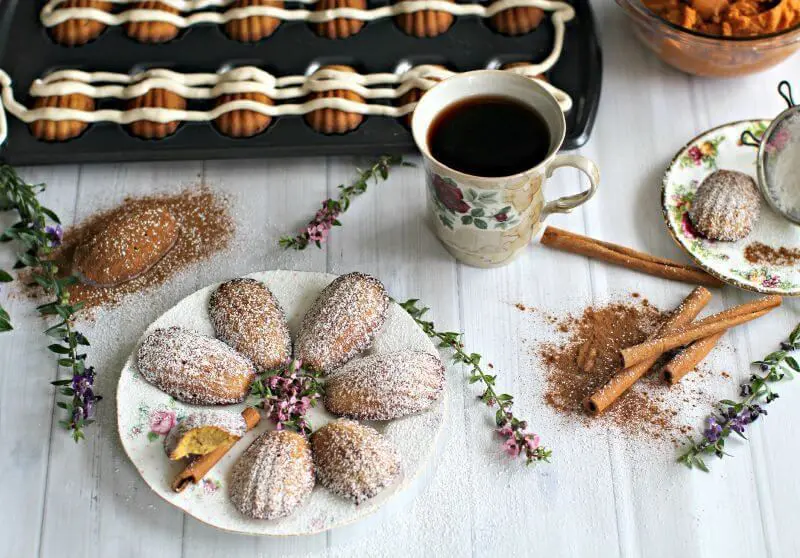 Pumpkin Madeleine next to a cup of coffee and cinnamon sticks on a table