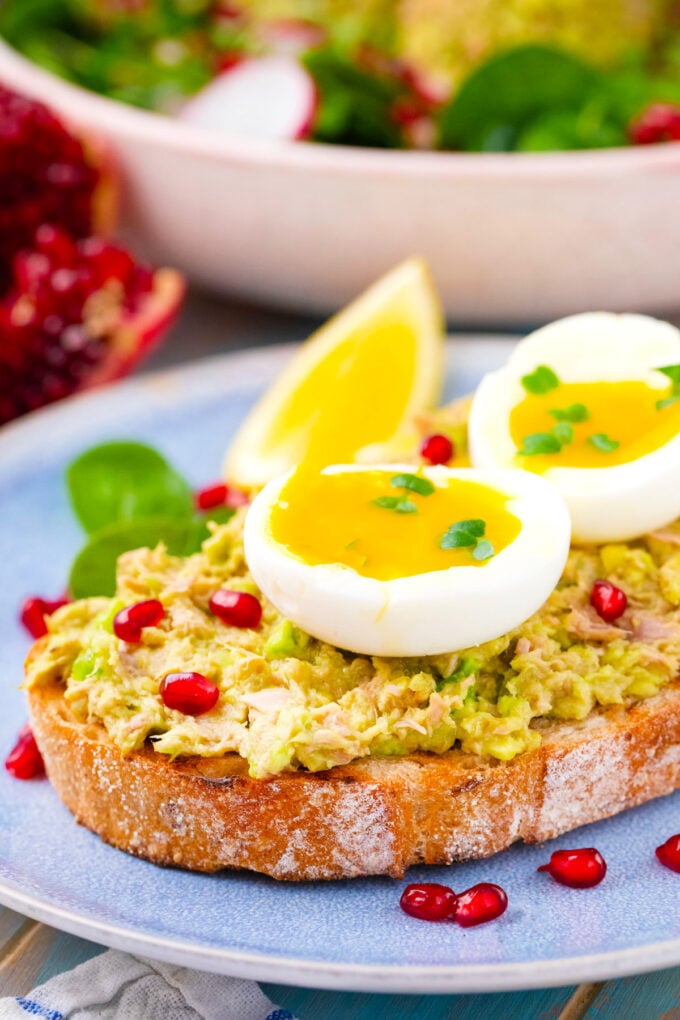 An avocado tuna salad sandwich topped with a runny egg and pomegranate seeds.