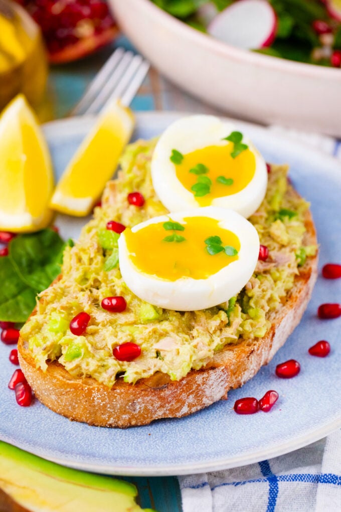 Creamy avocado tuna salad sandwich topped with a runny egg and pomegranate seeds.