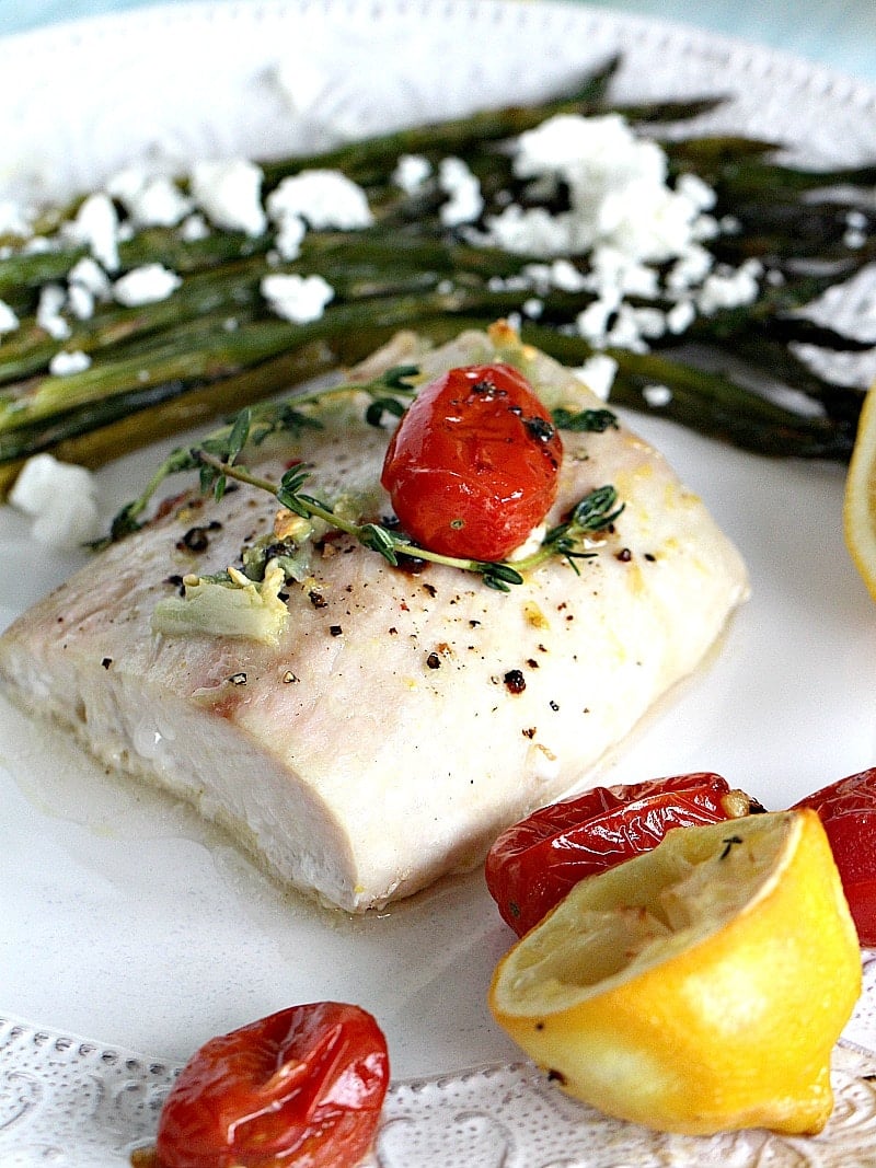 Image of oven roasted mahi mahi fish on a plate with asparagus, cherry tomato and lemon.