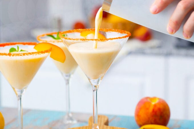 Pouring peaches and cream martini in martini glasses.