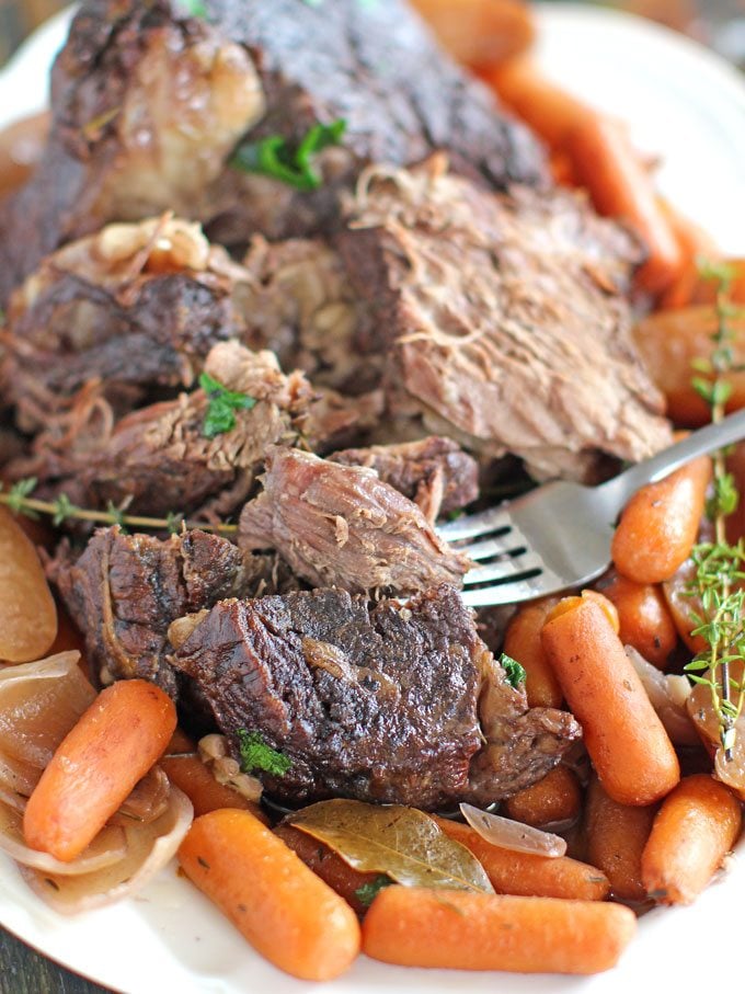 Image of slow cooker pot roast with carrots and potatoes on a white plate. 