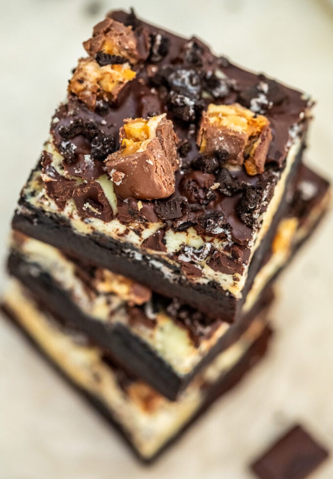 Image of fudgy brownies cheesecake bars topped with chopped snickers bars. 