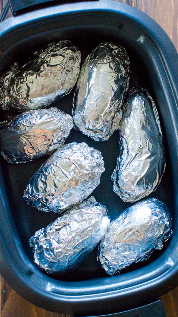 Whole potatoes wrapped in aluminium foil and placed in the crockpot for cooking