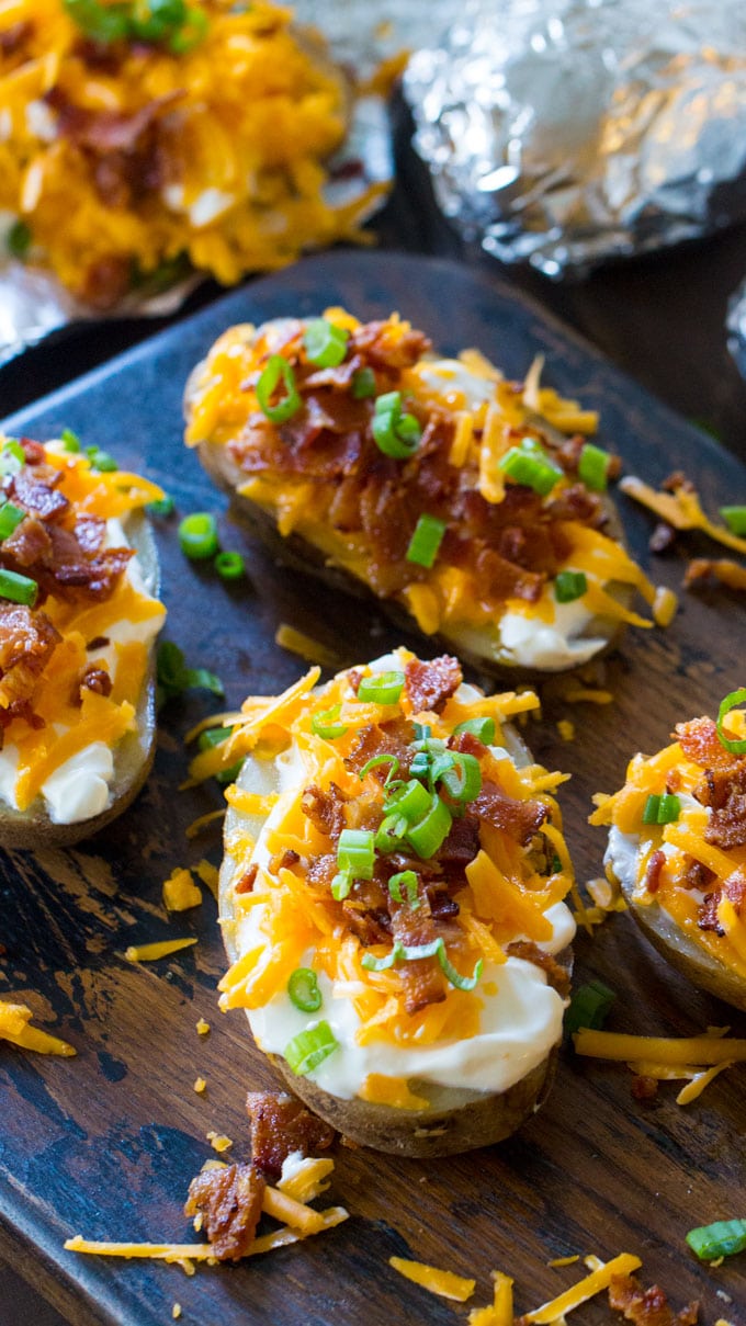 Loaded baked potatoes topped with shredded cheddar cheese, bacon and chopped red onion on a table