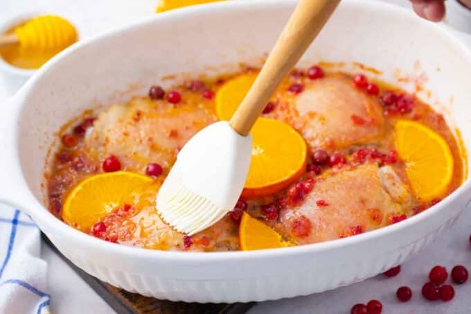 a pan with chicken thighs in cranberry orange sauce with fresh oranges