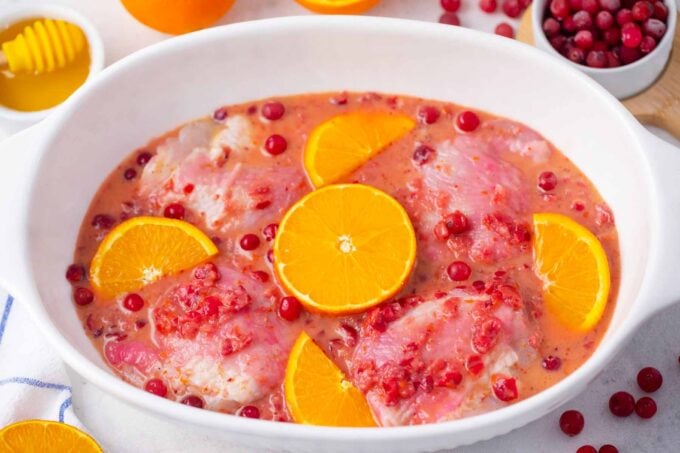 a pan with chicken thighs in cranberry orange marinade with fresh oranges