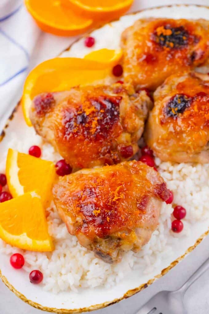 crispy oven baked cranberry orange chicken thighs served with rice and fresh oranges