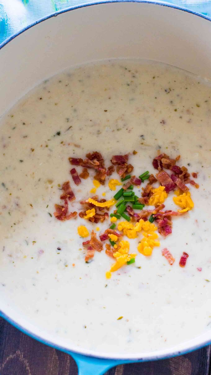 a pot of baked potato soup garnished with shredded cheese and bacon crumbs