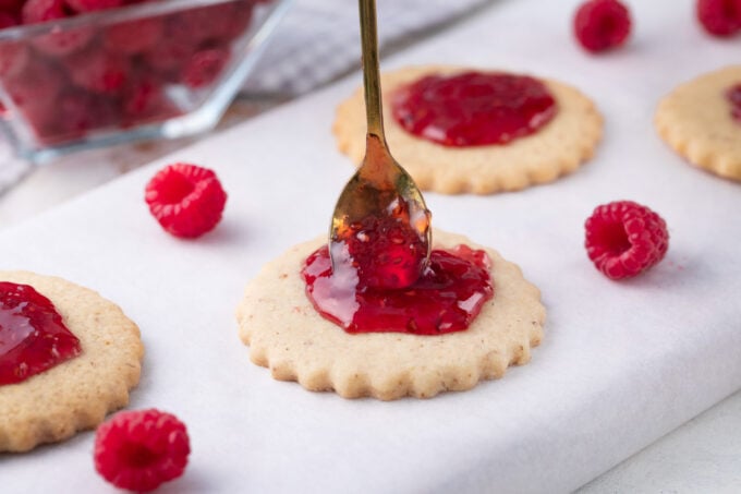 Adding raspberry preserves to Linzer cookies.