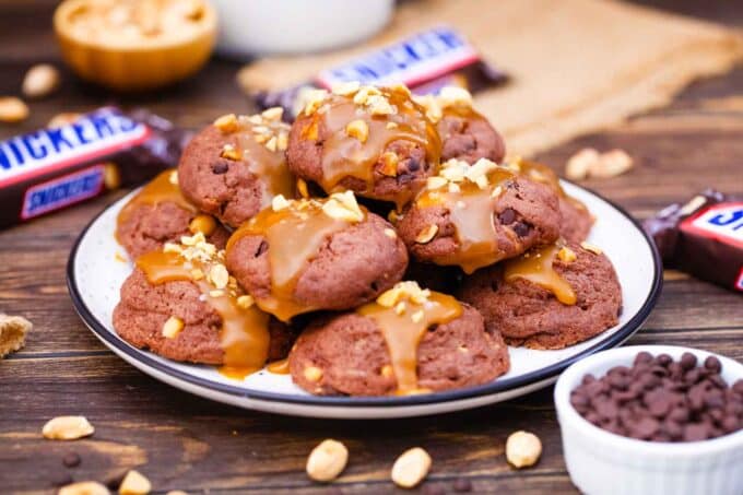 a stack of snickers cookies on a plate with snickers candy bar in the background