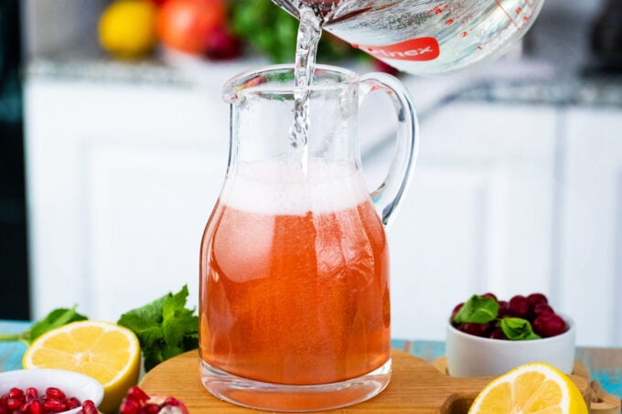 Pouring water into a pitcher with cranberry mocktail.