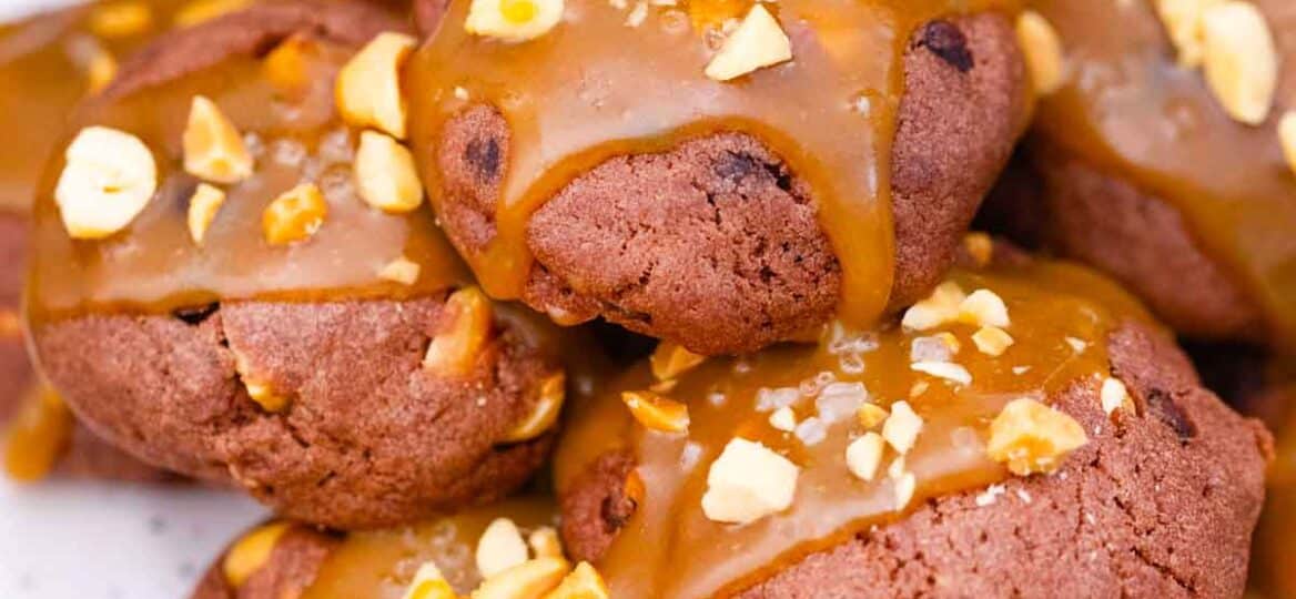 close shot of snickers cookies on a plate, topped with caramel sauce and peanuts