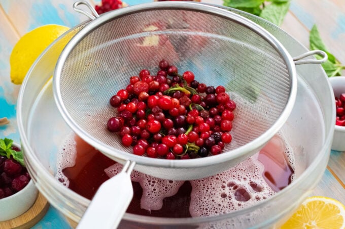 Straining cranberry simple syrup into a bowl.