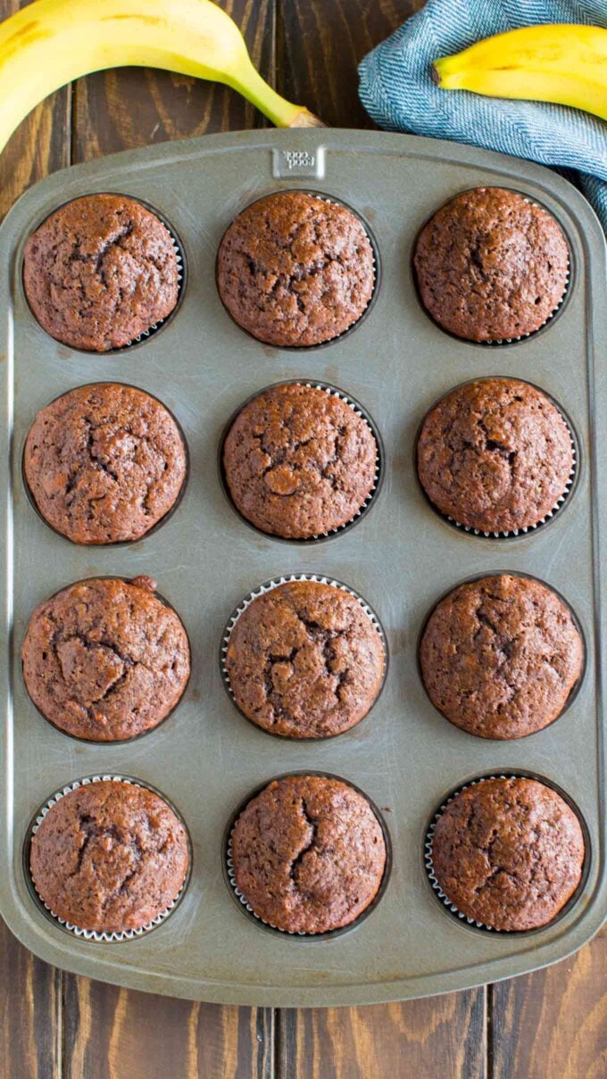 Photo of twelve chocolate banana muffins on a baking sheet.