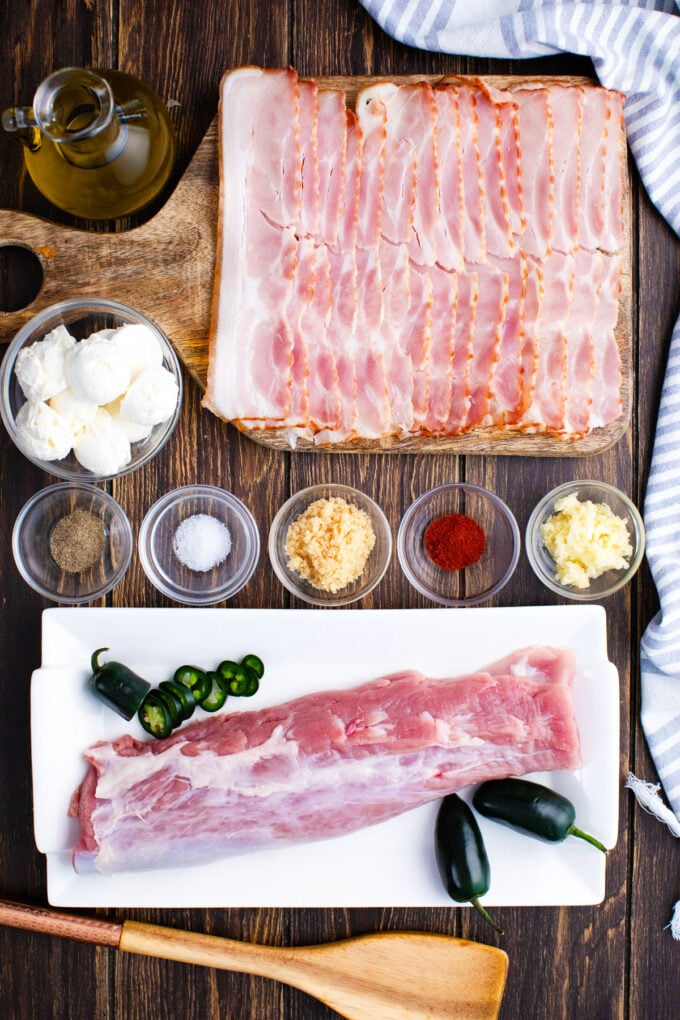 Overhead shot of bacon wrapped pork tenderloin ingredients arranged on a white sruface.