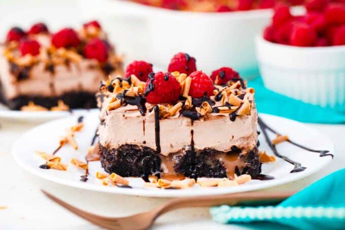 a slice of chocolate baileys poke cake topped with fresh raspberries and chocolate sauce