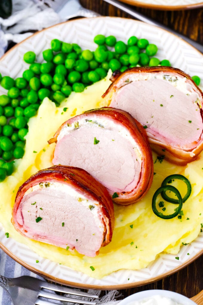 Sliced of bacon wrapped pork tenderloin with cream cheese over mashed potatoes.