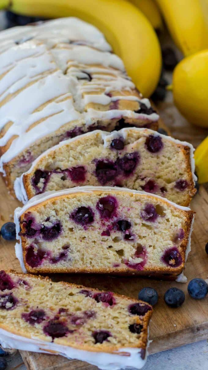 glazed blueberry banana bread on a cutting board with lemons and bananas in the background