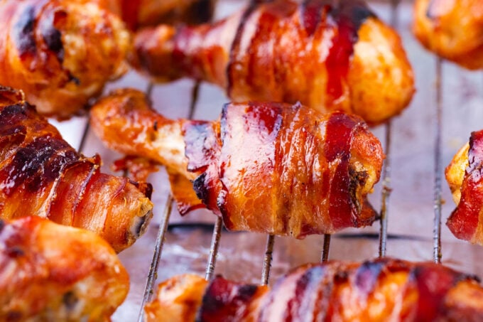 Crispy brown sugar bacon wrapped chicken drumsticks on a wire rack.