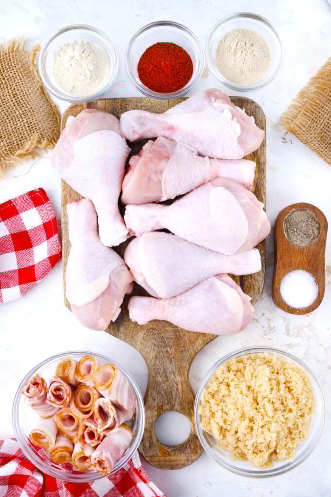 Overhead shot of brown sugar bacon wrapped chicken drumsticks ingredients arranged on a white surface.