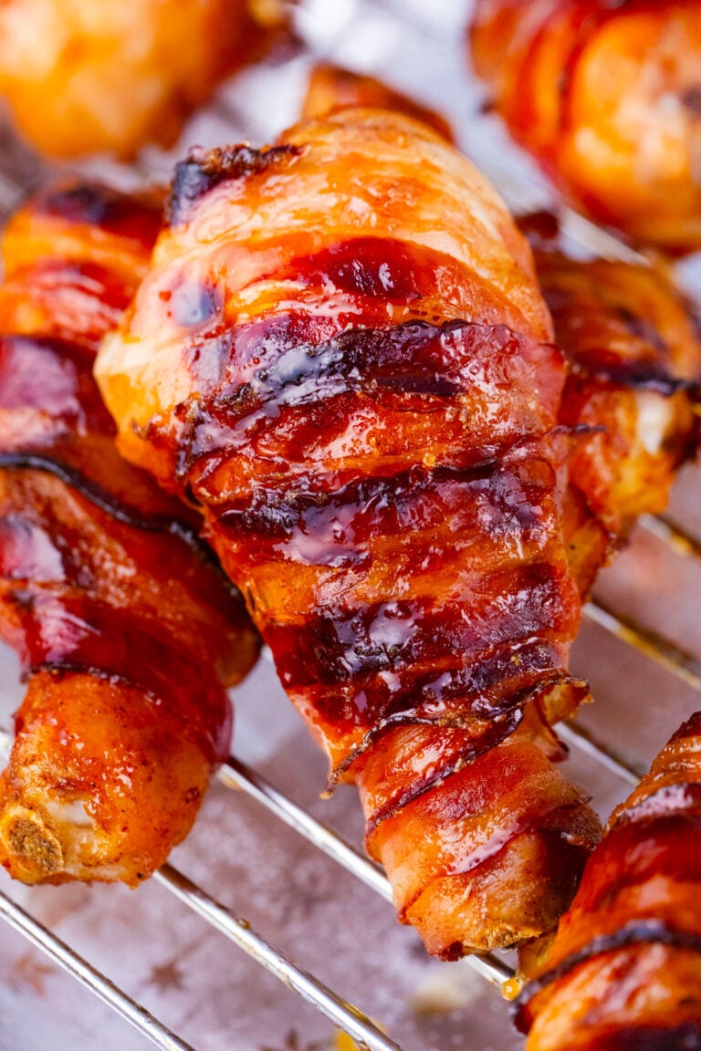 A stack of brown sugar bacon wrapped chicken drumsticks on a wire rack.