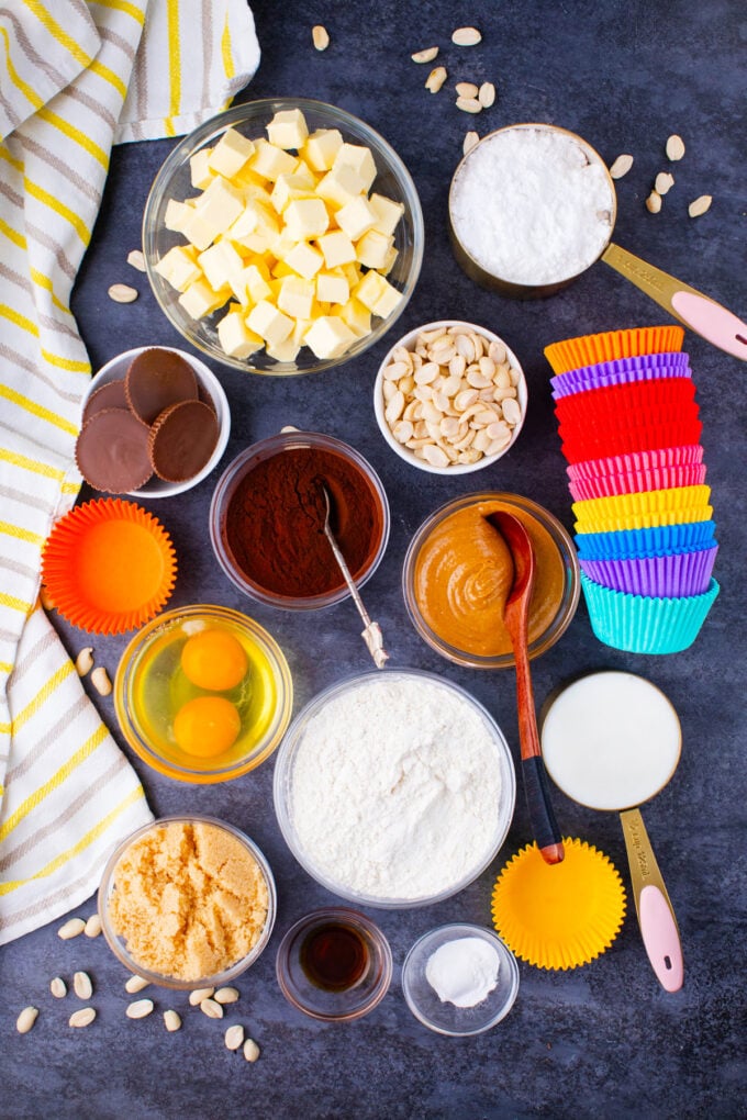 Overhead shot of dark chocolate peanut butter cupcake ingredients in bowls on a dark surface.