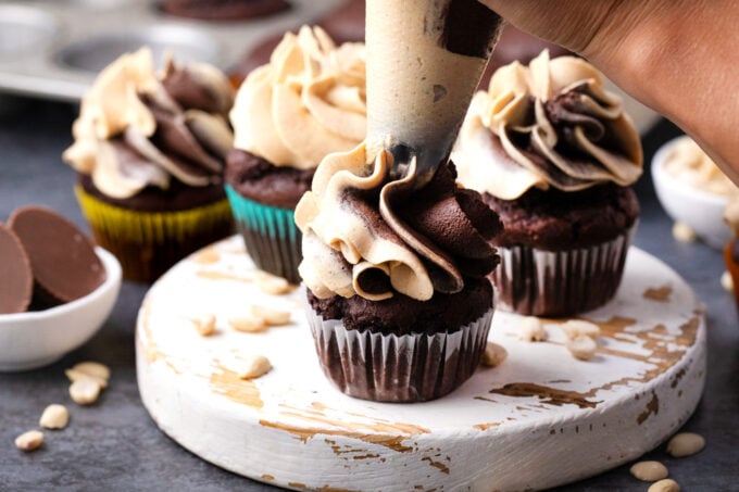Piping chocolate peanut butter frosting onto chocolate cupcakes.