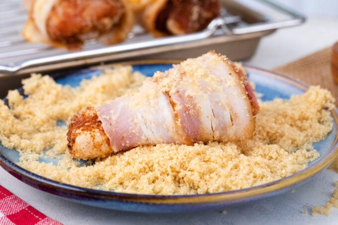 Rolling bacon wrapped chicken drumsticks in brown sugar.