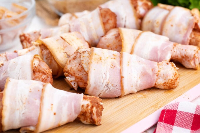 Brown sugar bacon wrapped chicken drumsticks arranged on a cutting board.
