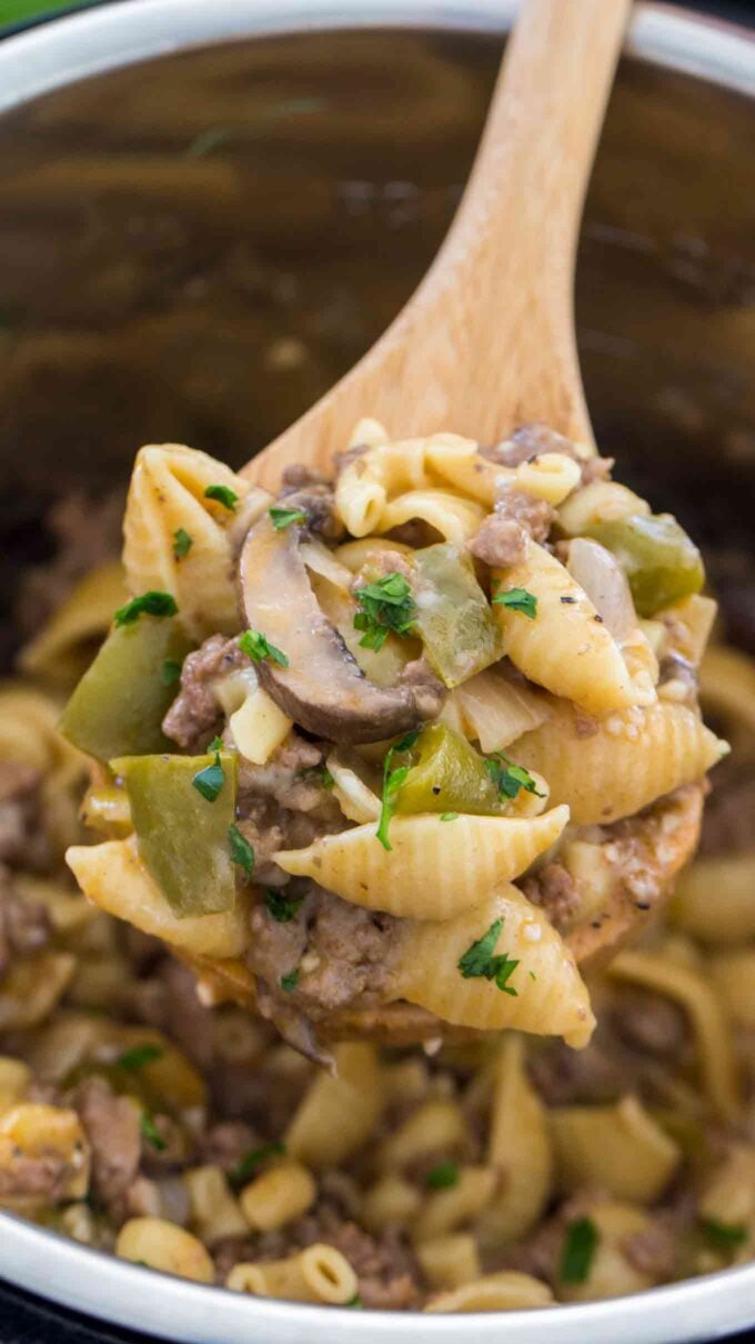 a wooden spoon filled with instant pot Philly cheesesteak pasta garnished with chopped parsley