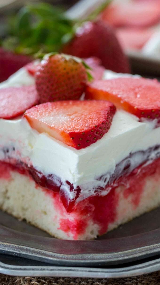 image of sliced strawberry poke cake topped with strawberries on a silver plate