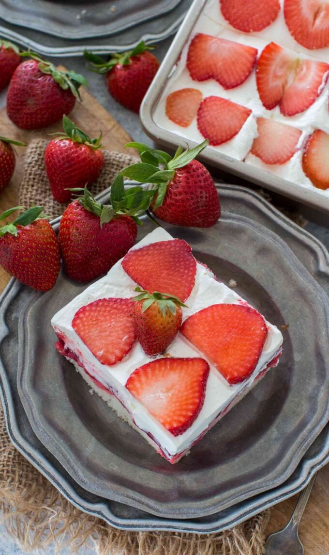 Homemade strawberry poke cake topped on a plate with fresh strawberries near it