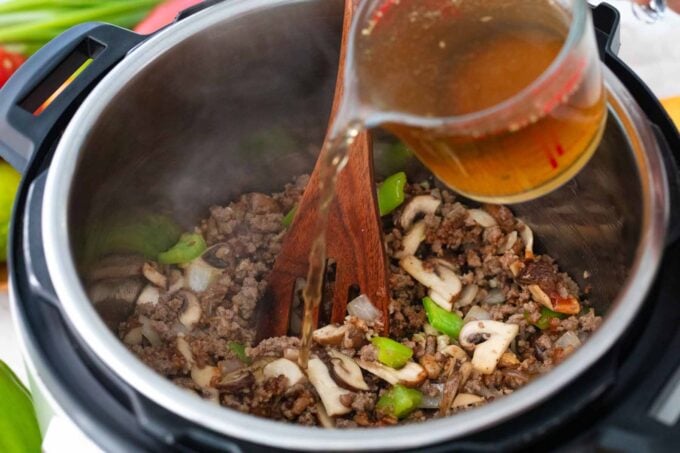 pouring broth over ground beef and veggies in the instant pot