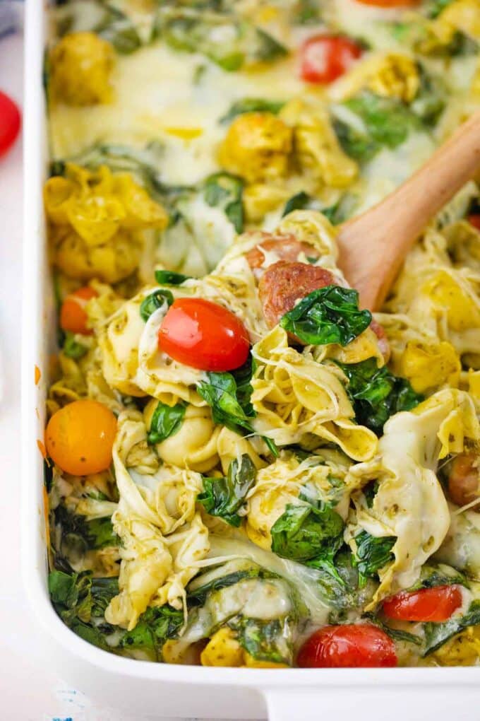 a large serving spoon of cheesy sausage pesto tortellini casserole