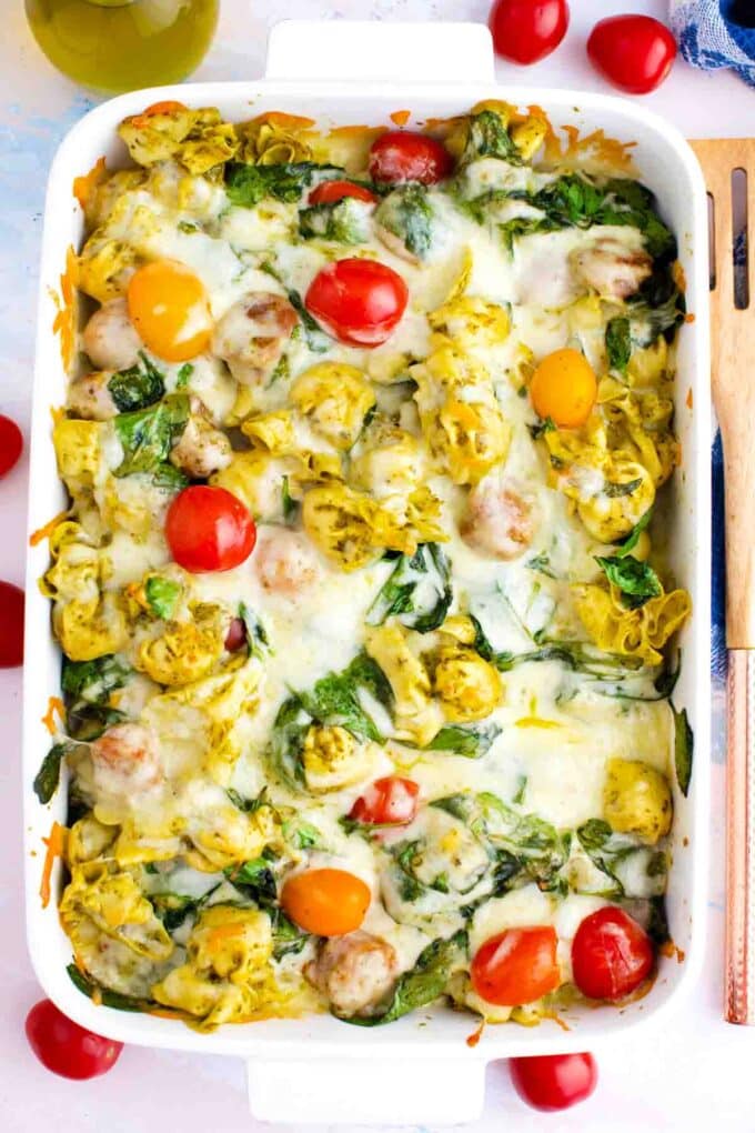 cheesy sausage pesto tortellini casserole in a baking dish topped with tomatoes