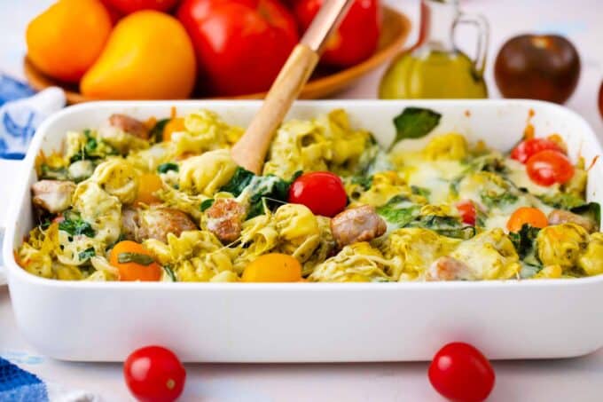 sausage pesto tortellini casserole with a plate of tomatoes in the background