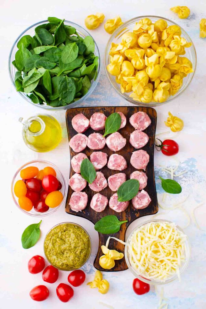 sausage pesto tortellini casserole ingredients arranged in bowls on a table