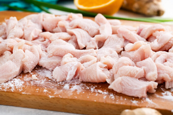 Cornstarch covered chicken pieces on a cutting board.