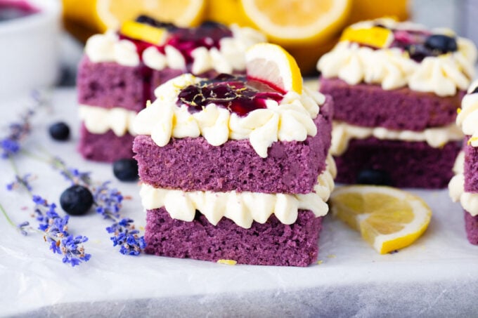 Individual purple cakes topped with lemon buttercream, lemon, and blueberry sauce.