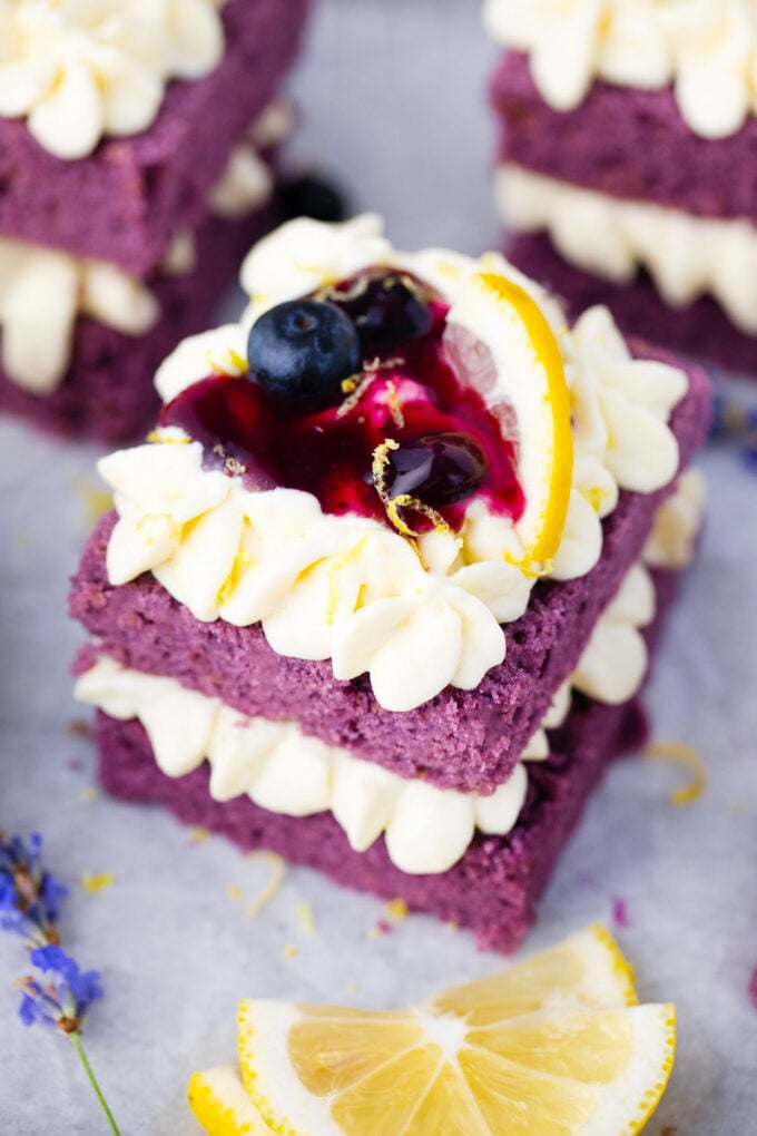 Purple cake topped with lemon buttercream, lemon, and blueberry sauce.