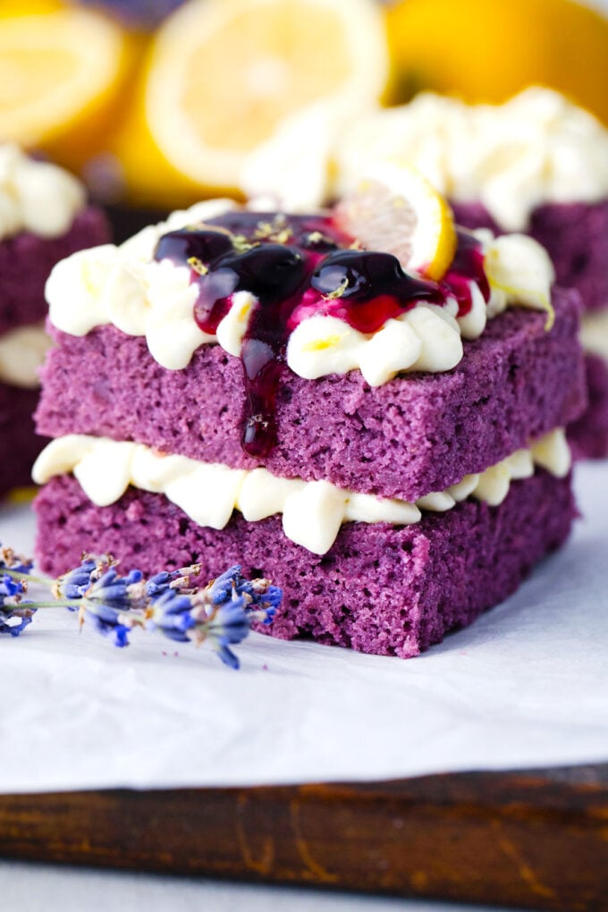 Purple cake topped with lemon buttercream and blueberry sauce dropping on the sides.