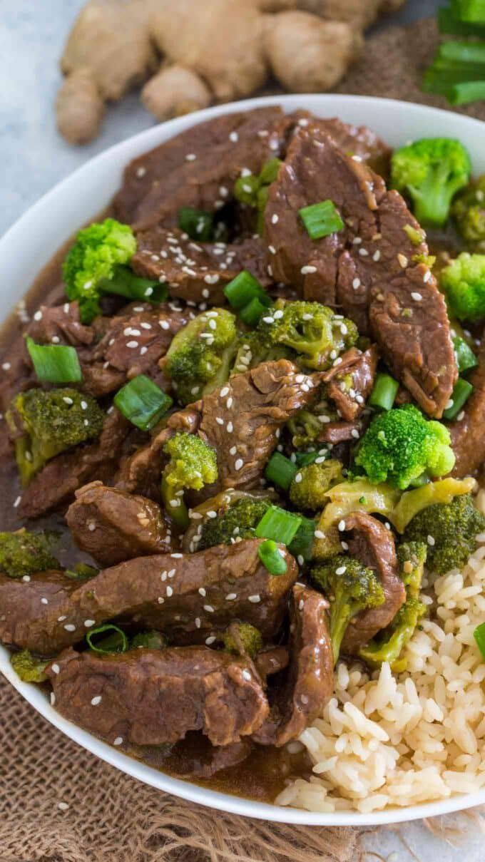 beef and broccoli garnished with sesame seeds and rice on a plate