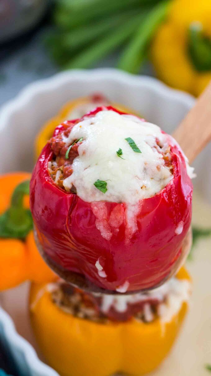 red stuffed pepper with beef and rice topped with melted cheese and chopped parsley on a wooden spoon