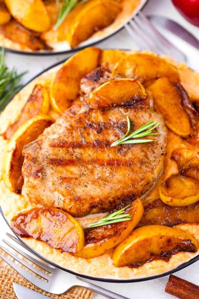 grilled apple cinnamon pork chops with juicy cinnamon apple slices and rosemary sprigs on top of mashed sweet potatoes